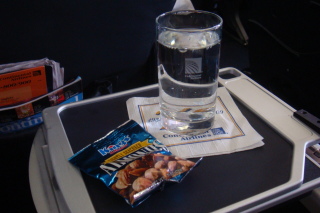 a glass of water and a packet of nuts on a tray