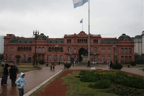 a pink building with a flagpole in front of it with Casa Rosada in the background