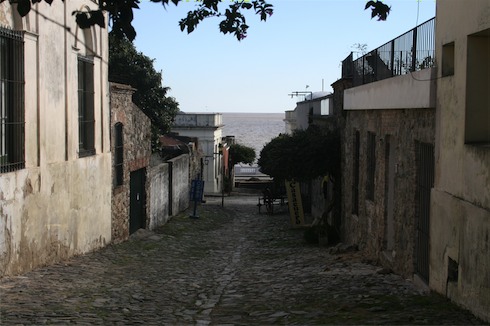 a stone alleyway with buildings and a body of water in the background