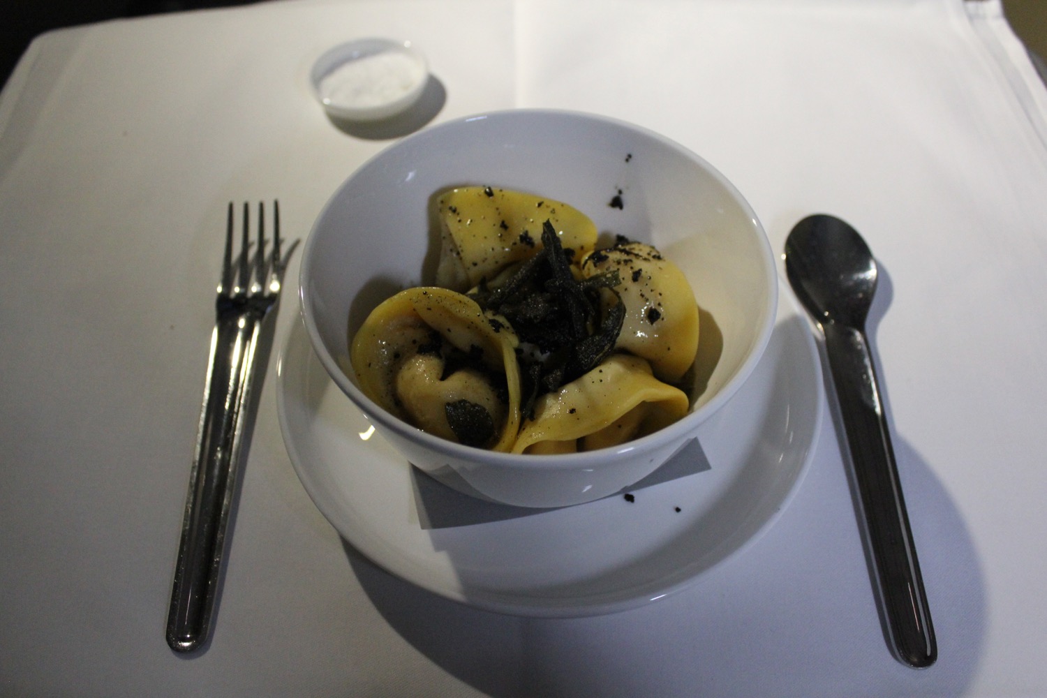 a bowl of pasta with black specks on top and a spoon
