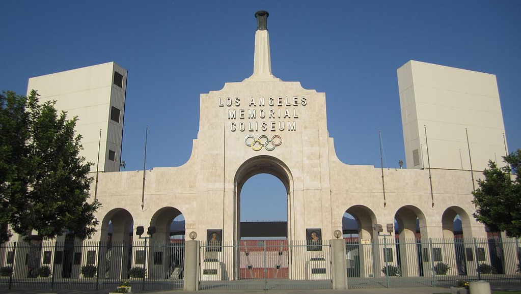 a large stone building with a sign on it with Los Angeles Memorial Coliseum in the background