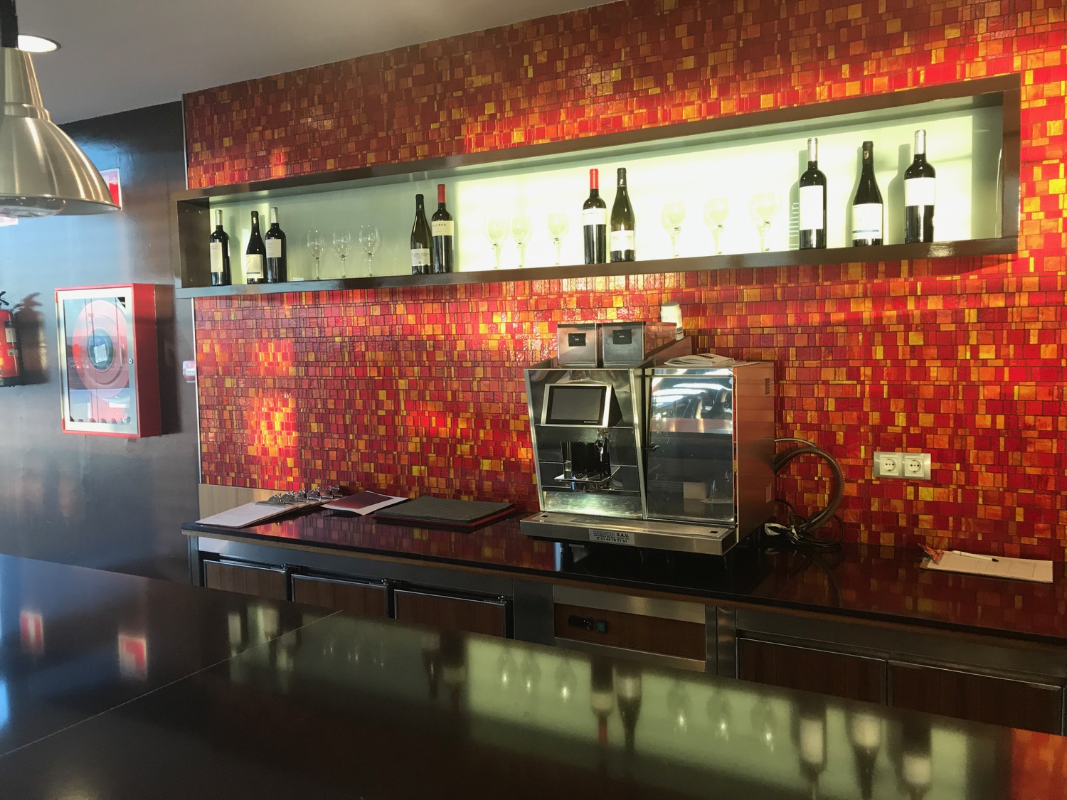 a counter with a coffee machine and bottles of wine on the wall