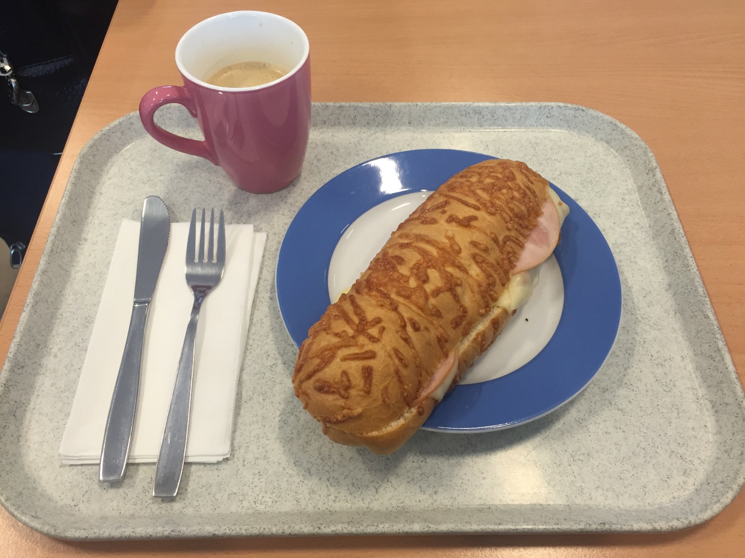 a sandwich on a plate with a cup of coffee and silverware on a tray