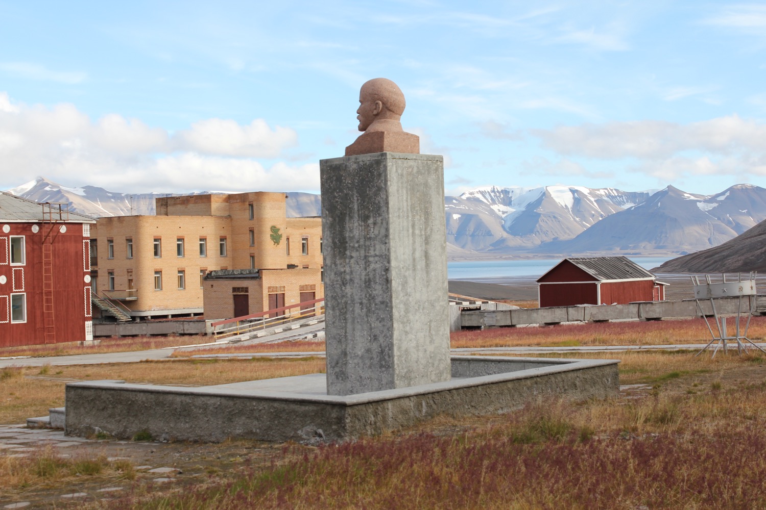 a statue of a man on a pedestal in a field with buildings and mountains in the background