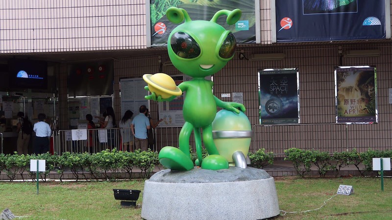 a green alien statue in front of a building