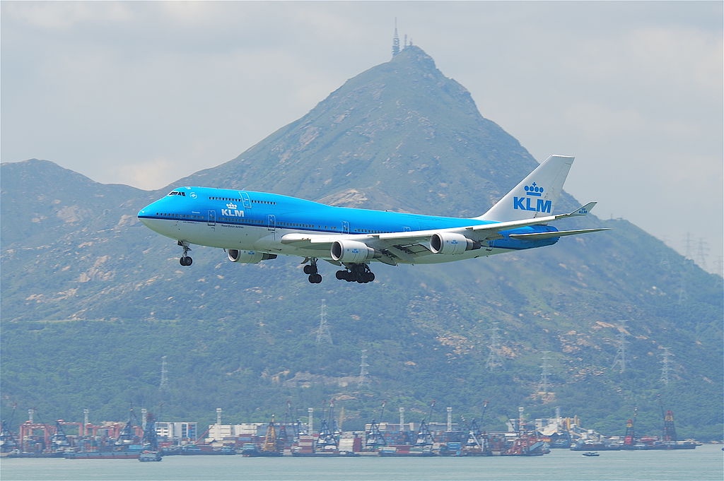 a blue and white airplane flying over water with mountains in the background