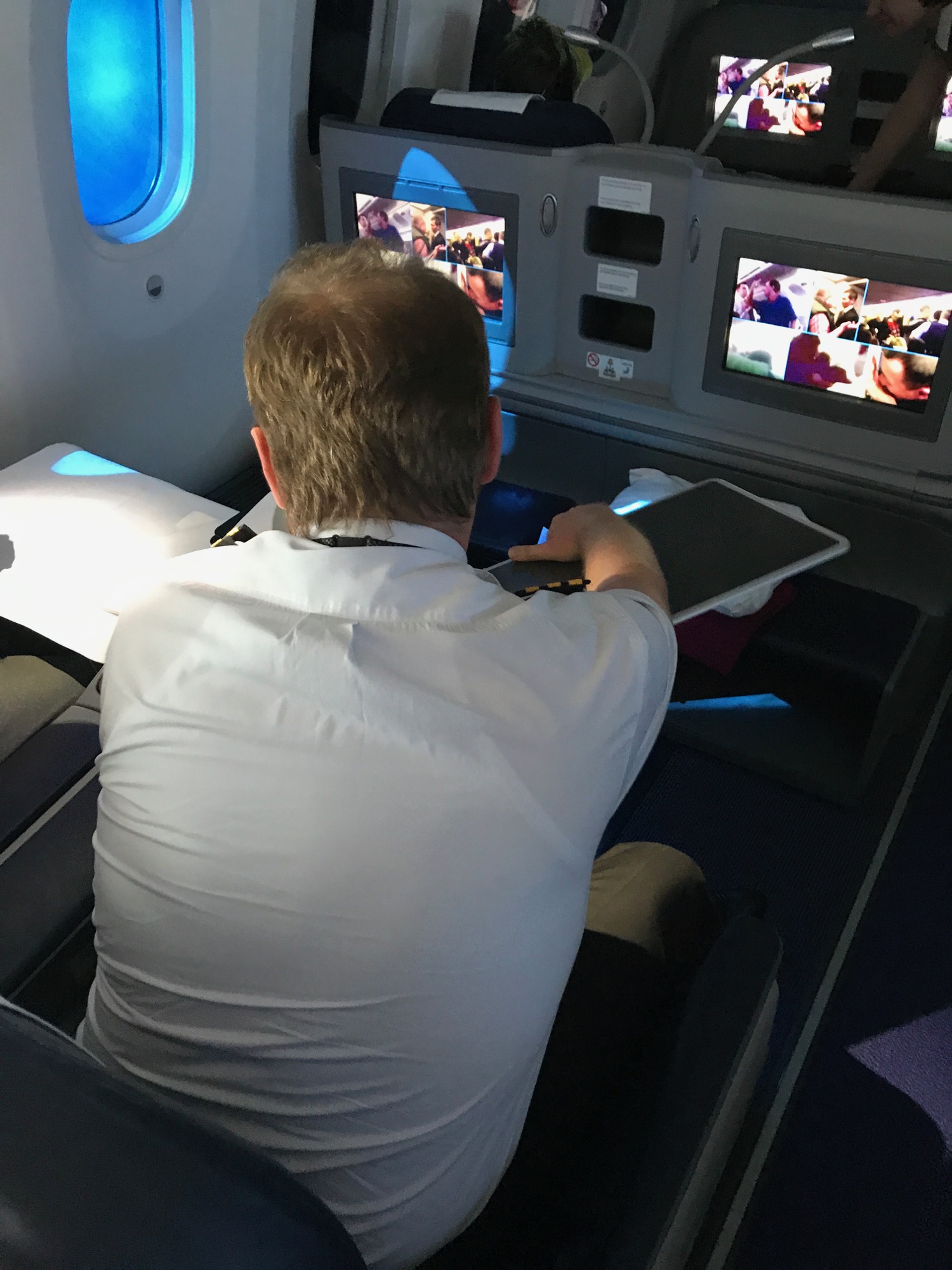 a man sitting in an airplane with a tablet and two monitors