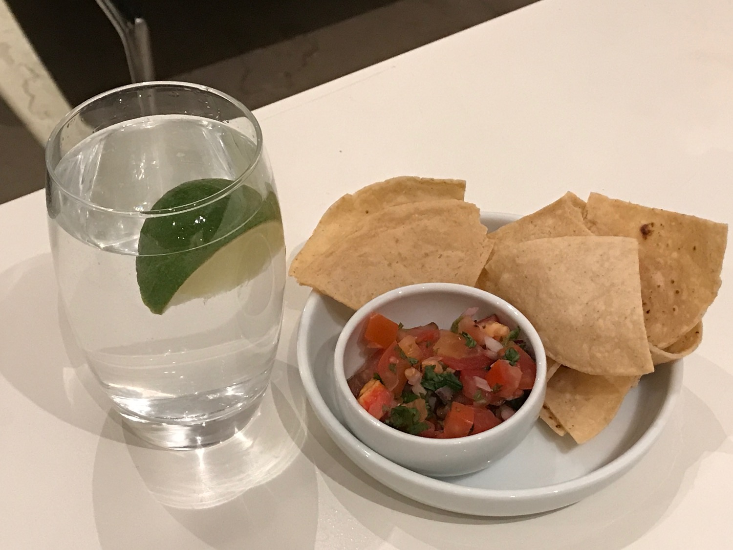 a plate of chips and salsa on a white plate next to a glass of water