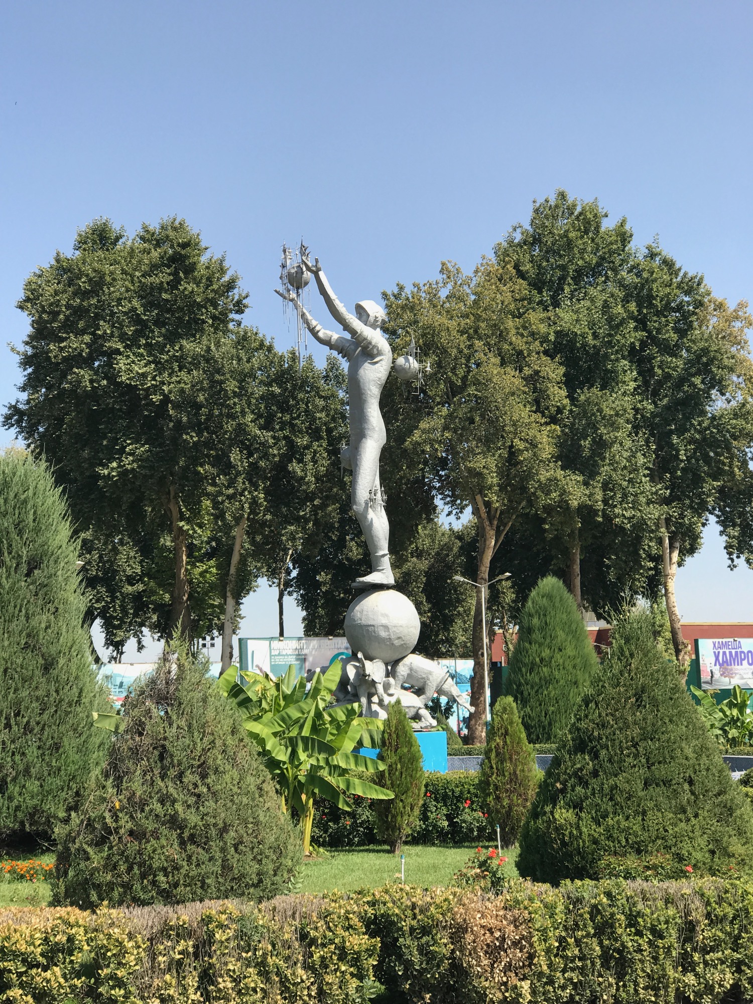 a statue of a man holding a ball and a ball with trees in the background