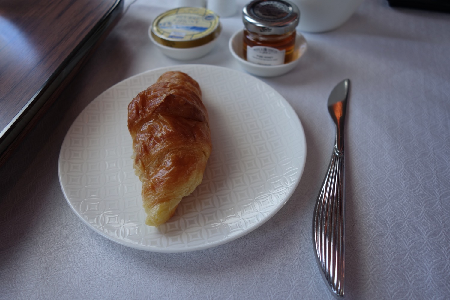 a croissant on a plate next to a knife and butter