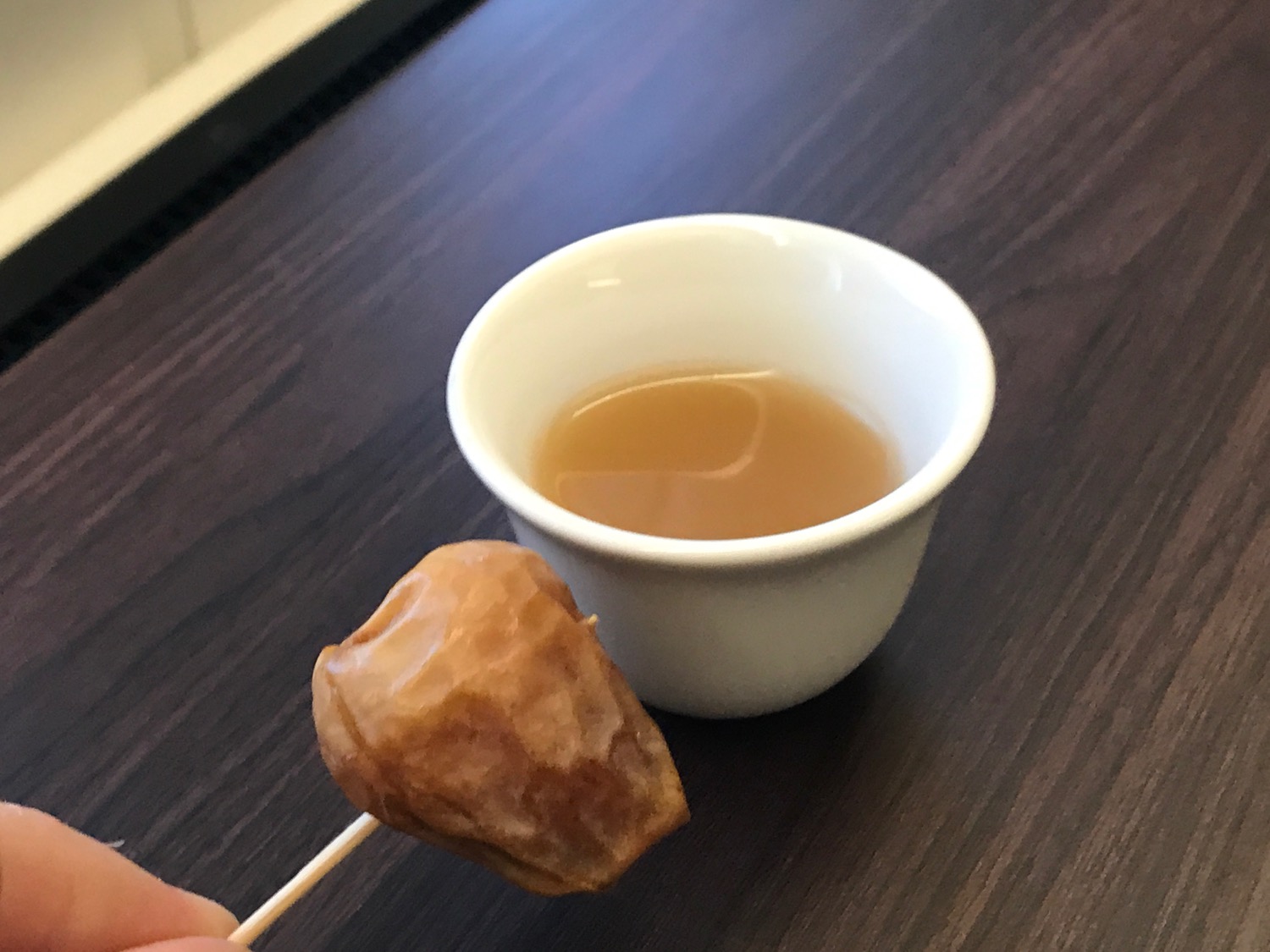 Hand holding a stick with food on a stick next to a cup with liquid