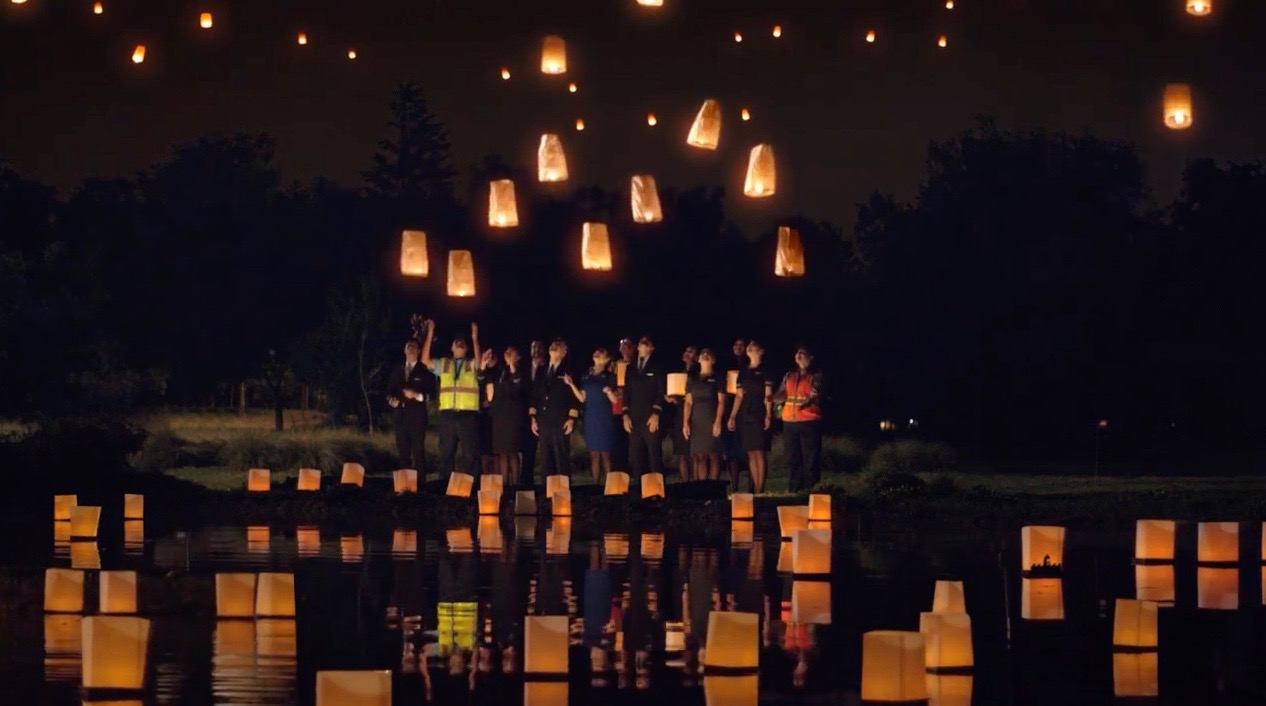 a group of people standing in front of a body of water with lanterns floating in the air