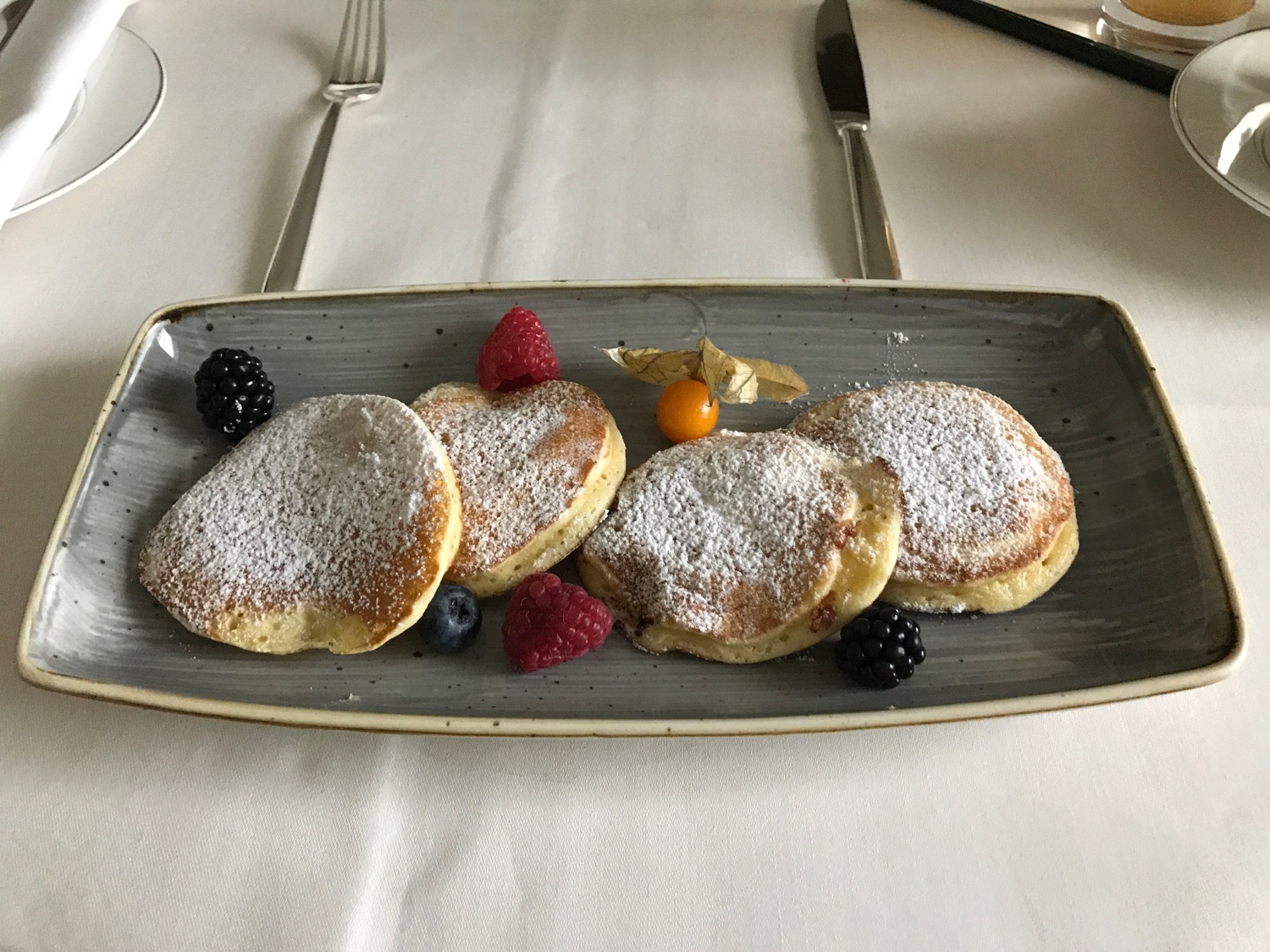 a plate of pancakes with berries and powdered sugar