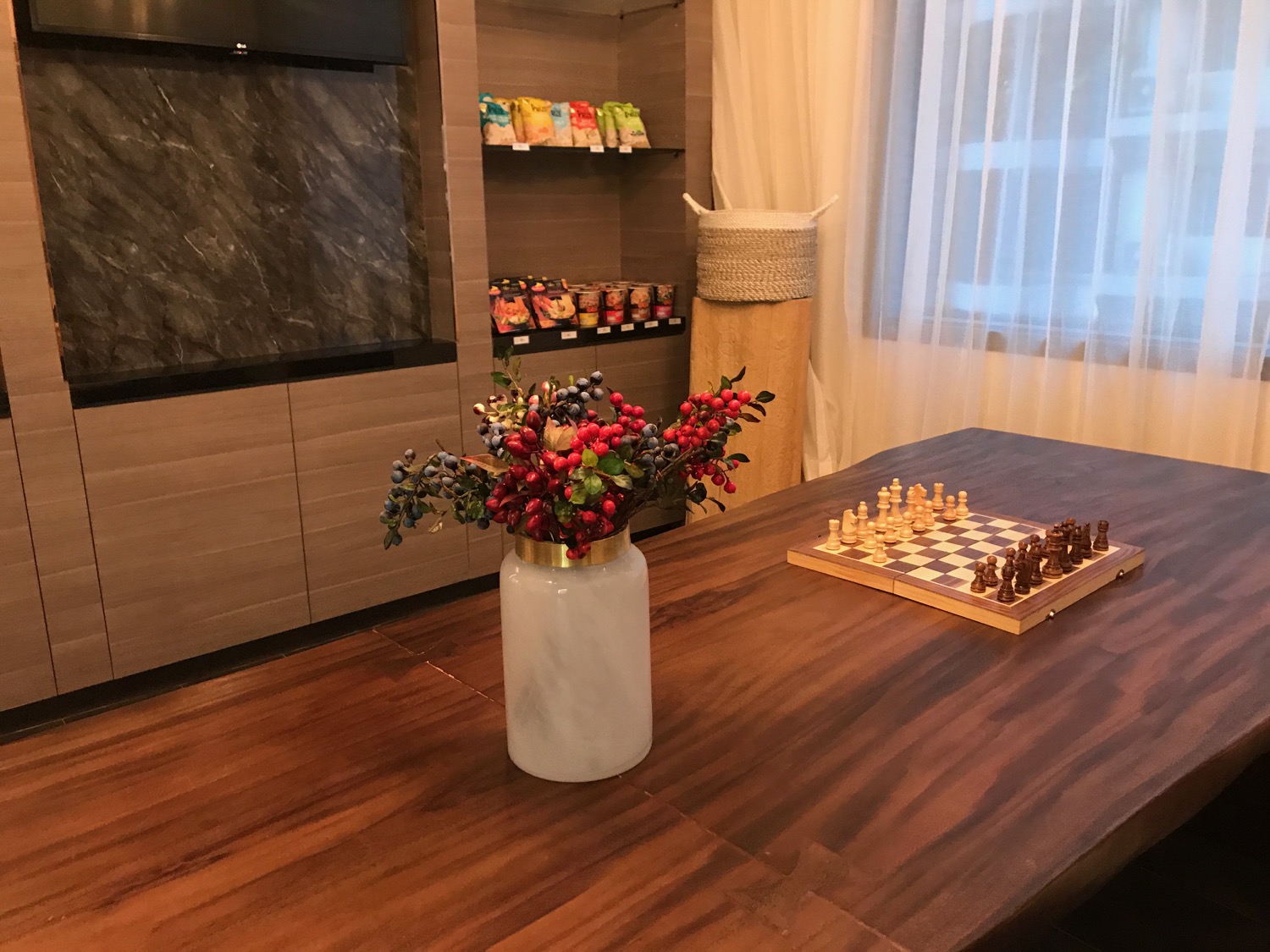 a vase with flowers on a table with chess board and a tv