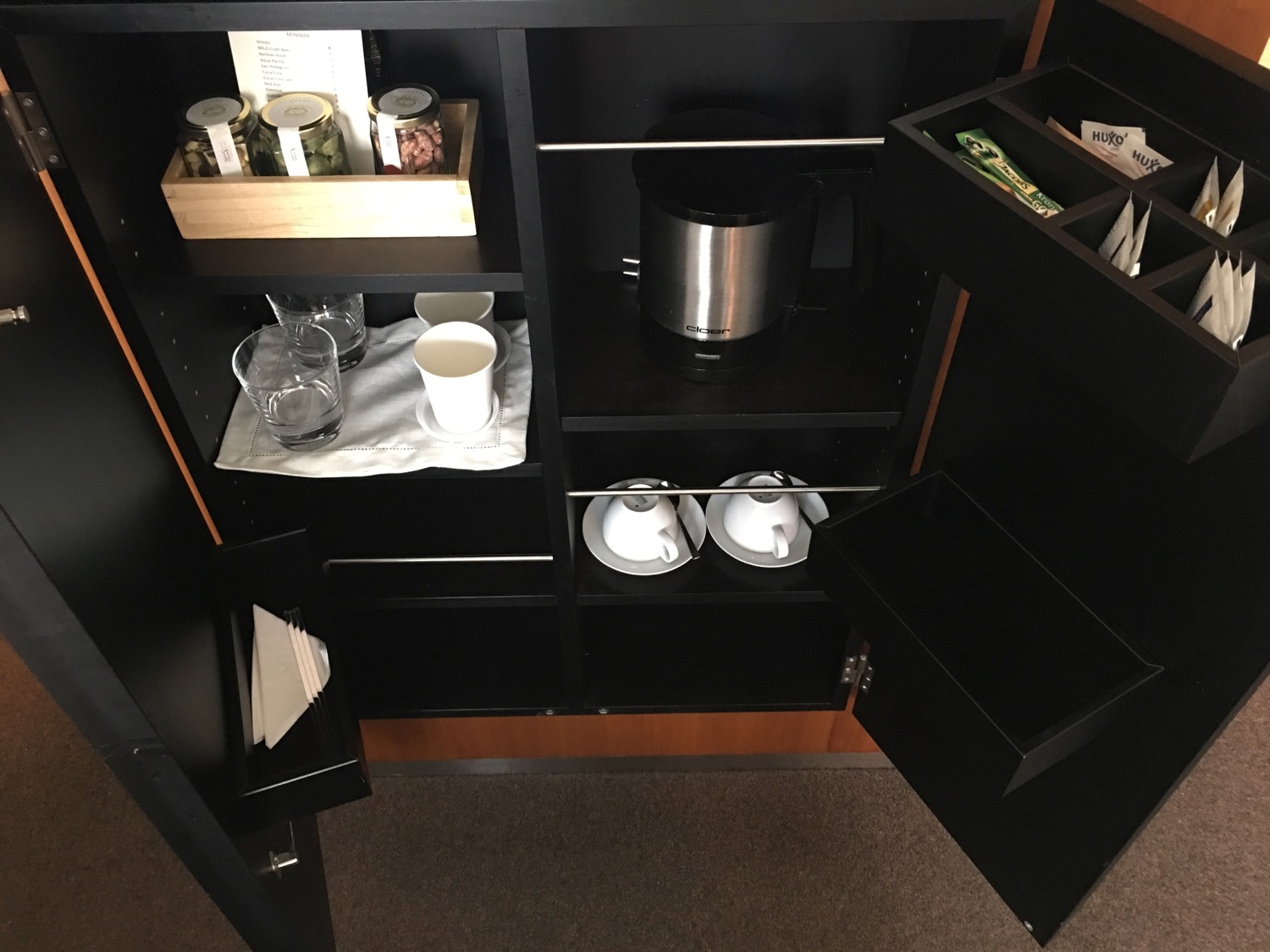 a black cabinet with a black shelf with a silver coffee maker and cups