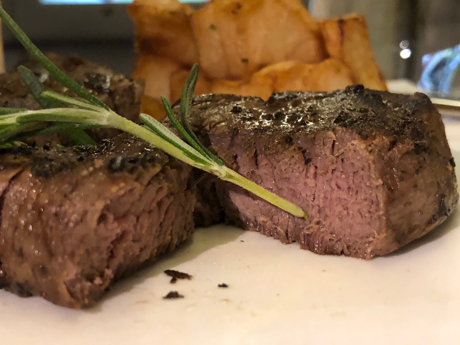 a piece of steak with a sprig of rosemary on a plate