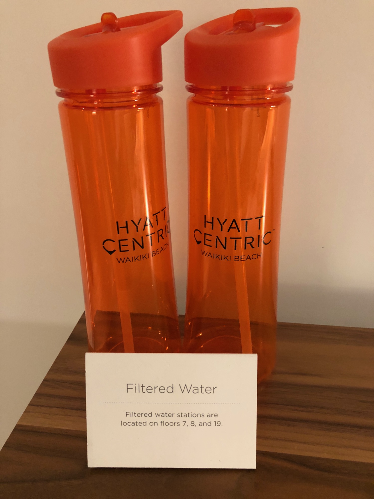 two orange water bottles with straws and a white sign