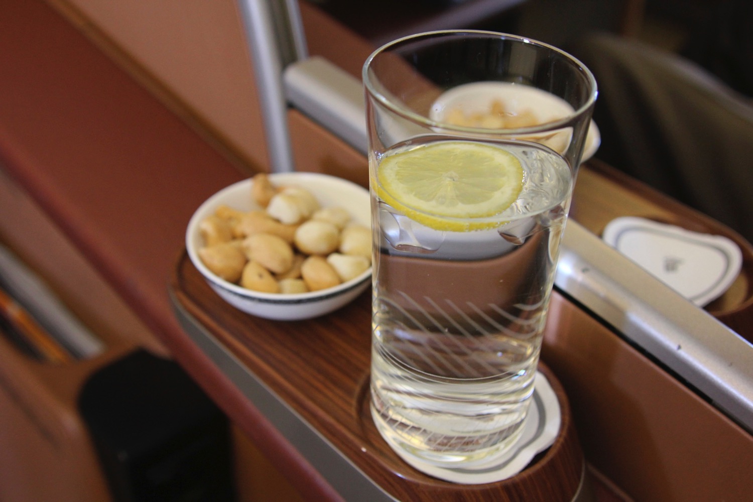 a glass of water with a lemon slice and a bowl of nuts