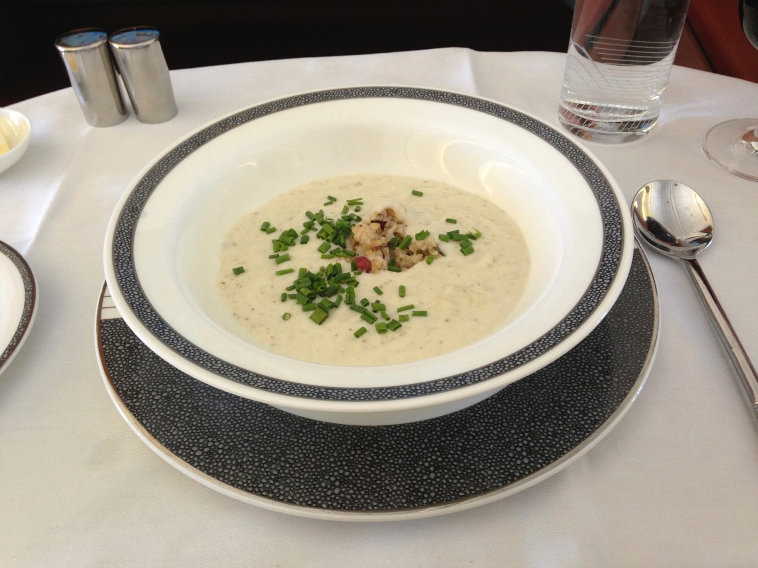 a bowl of soup with chives and a glass of water