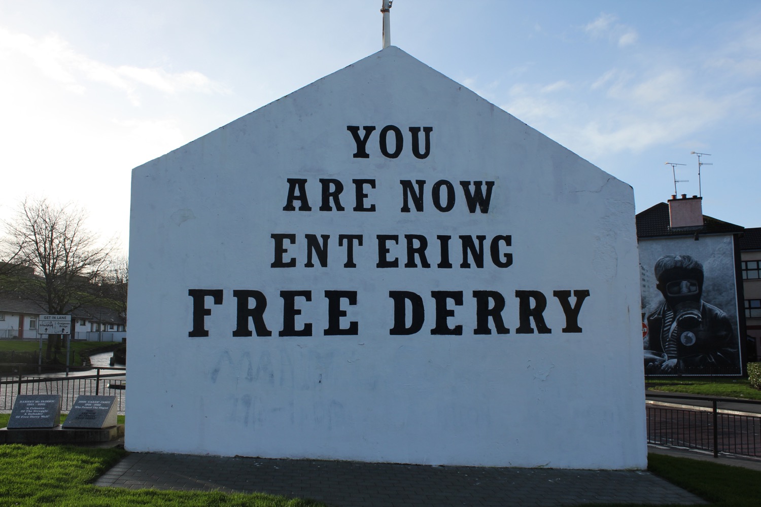 a white building with black text on it with Free Derry Corner in the background