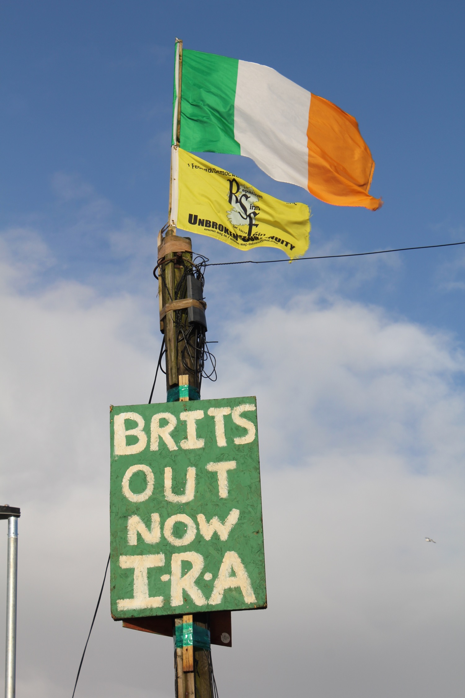 a green sign with white text and three flags on top of it