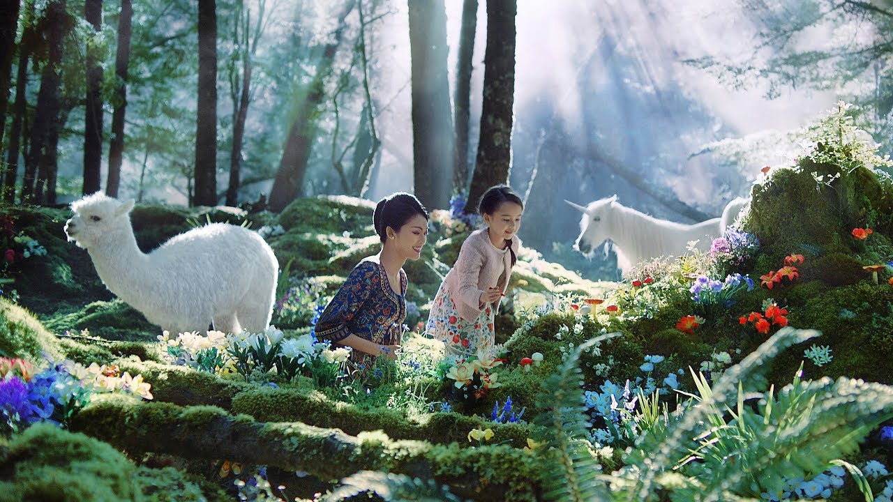 a woman and a girl standing in a forest with a unicorn