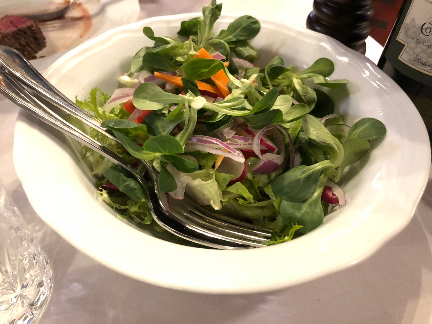 a bowl of salad with fork and knife