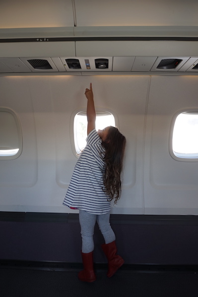 Lucy standing in the back of the plane in an unused section, she could nearly reach the reading light. 
