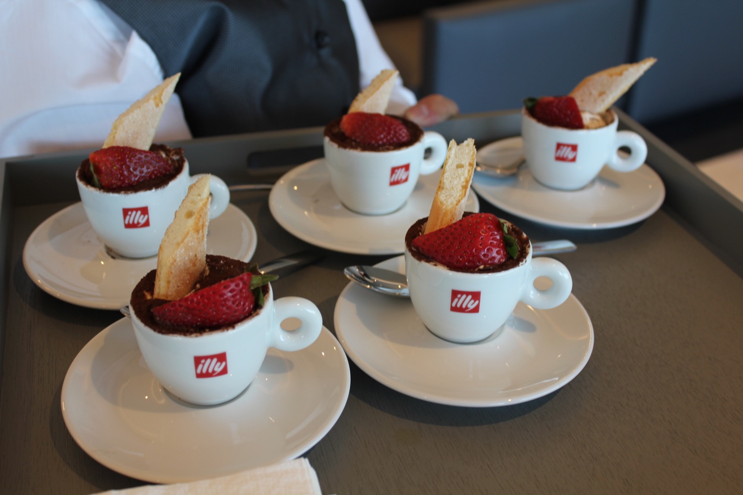 a group of small white cups with strawberries and a piece of bread on saucers