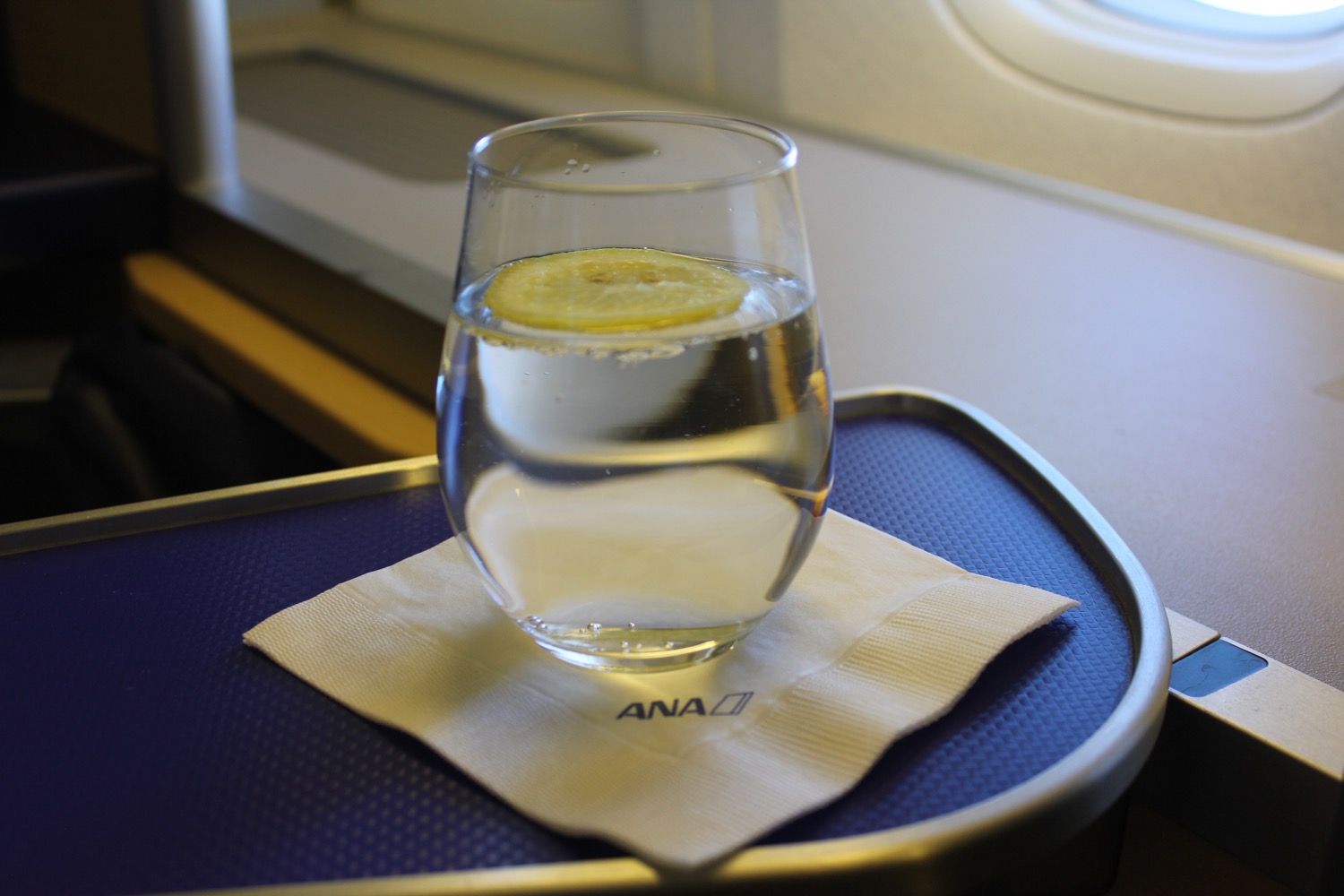 a glass of water with a slice of lemon on a napkin on a tray
