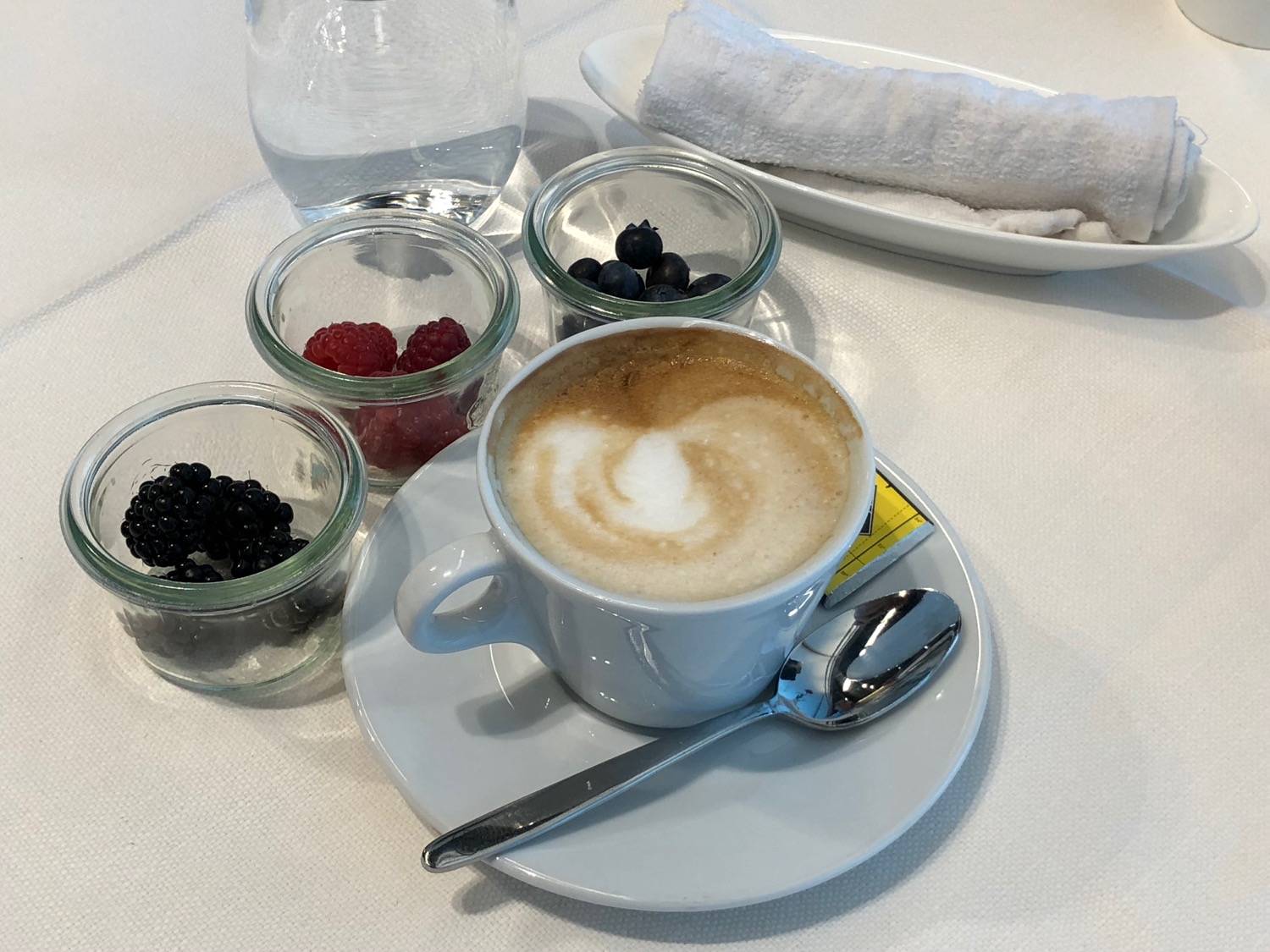 a cup of coffee with a heart on top and a spoon on a plate with berries