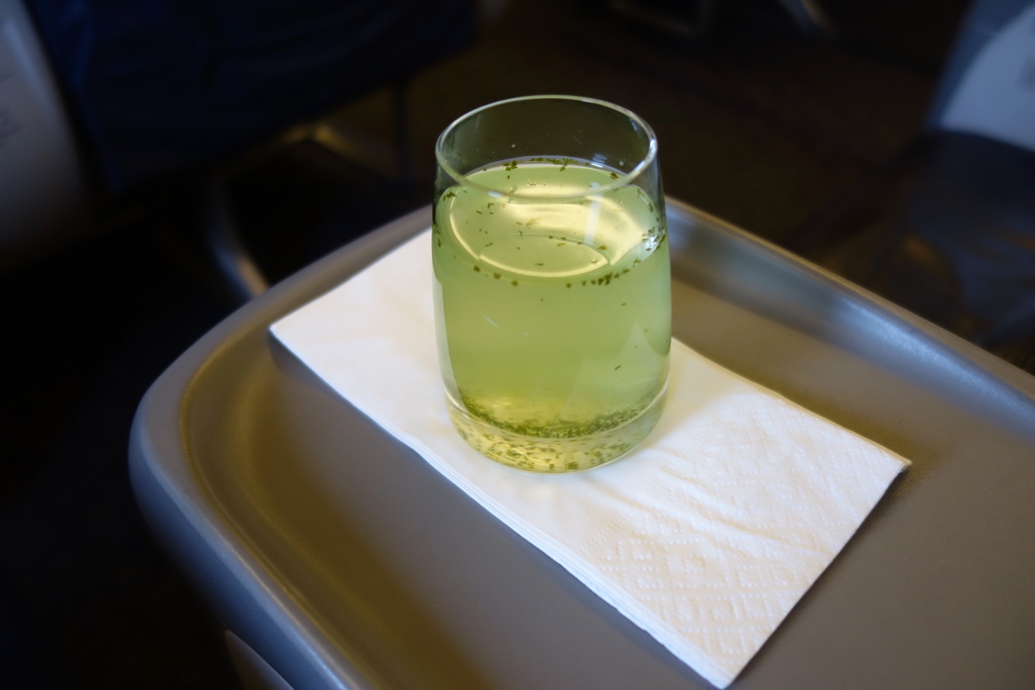a glass of green liquid on a napkin on a tray