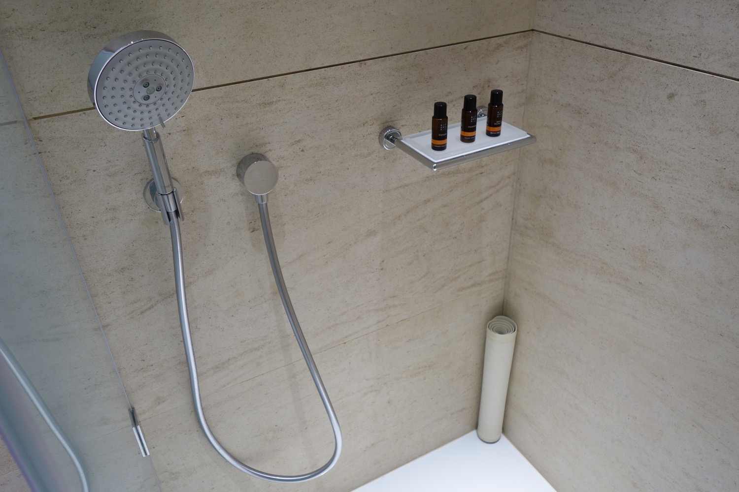 a shower with a shower head and a shelf with small bottles of essential oils