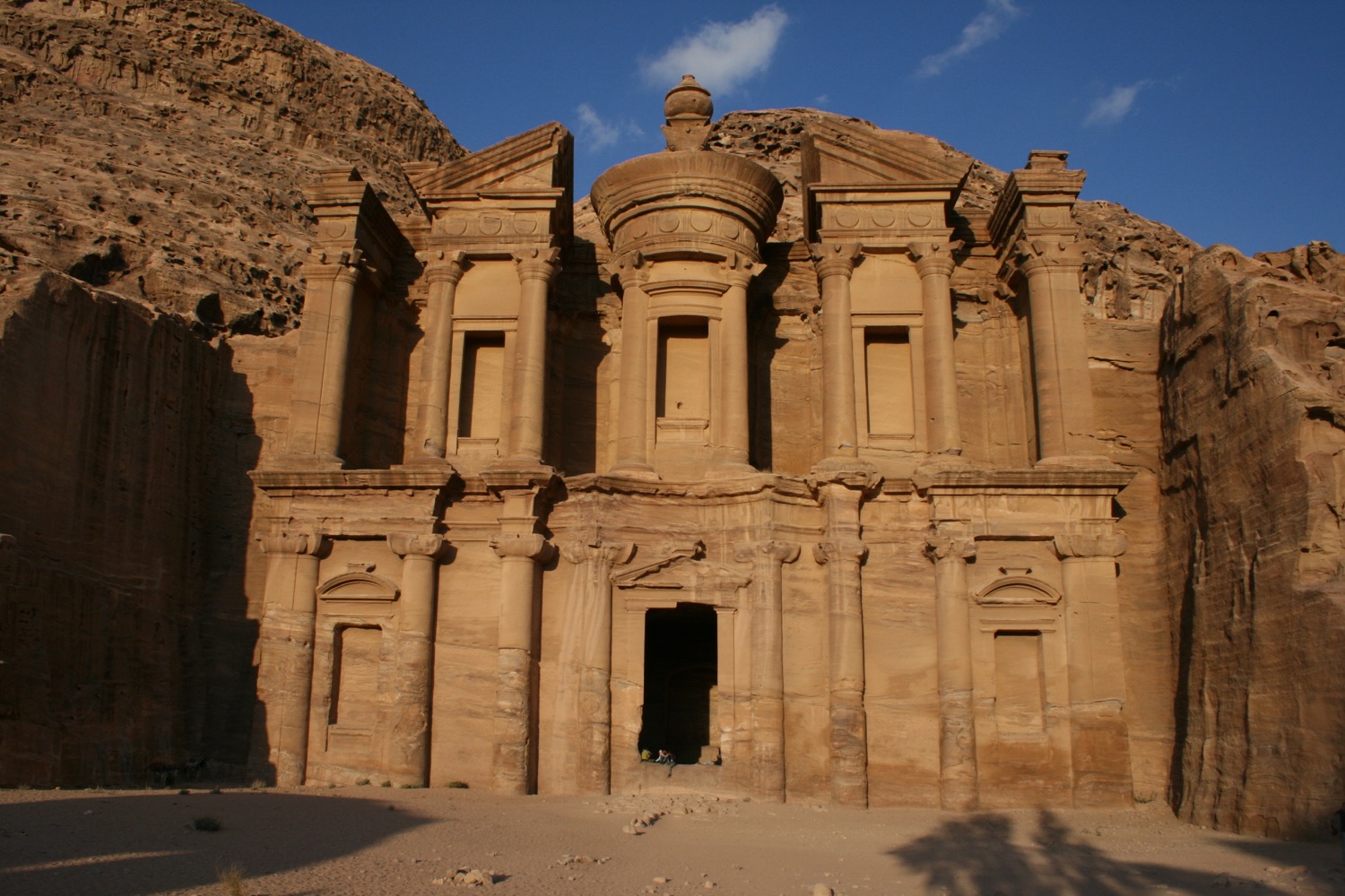 a stone building with columns and a roof with Petra in the background