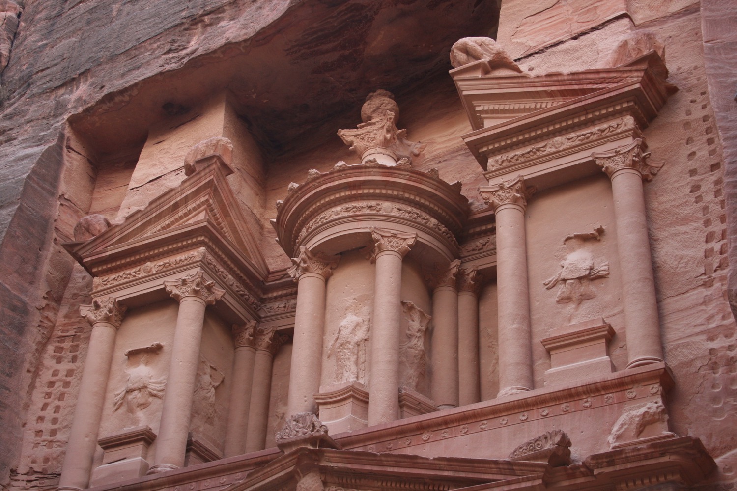 a stone building with pillars and statues with Petra in the background