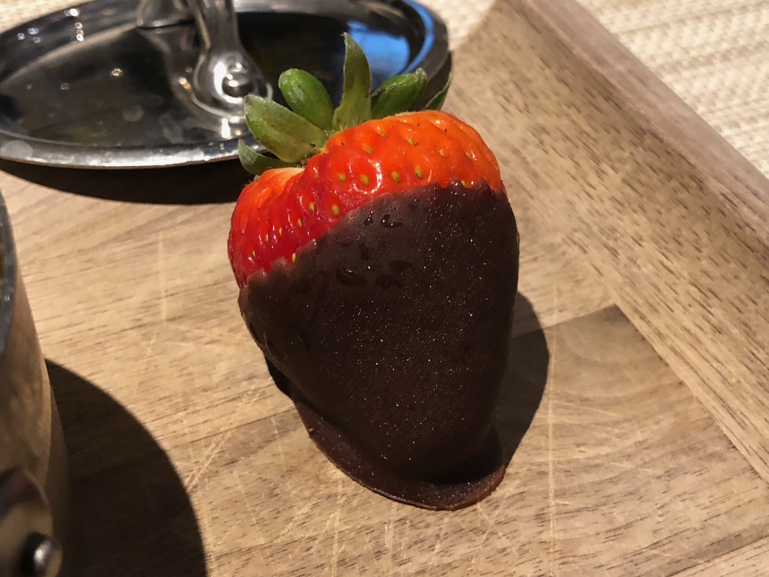 a chocolate covered strawberry on a wooden surface
