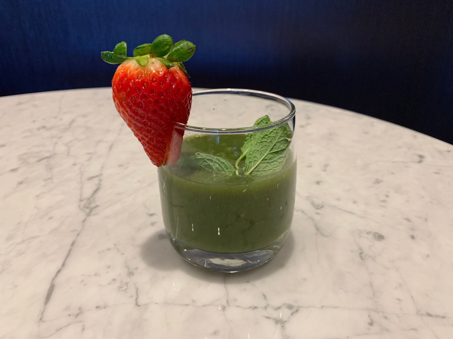 a glass with a strawberry on top and a green liquid with mint
