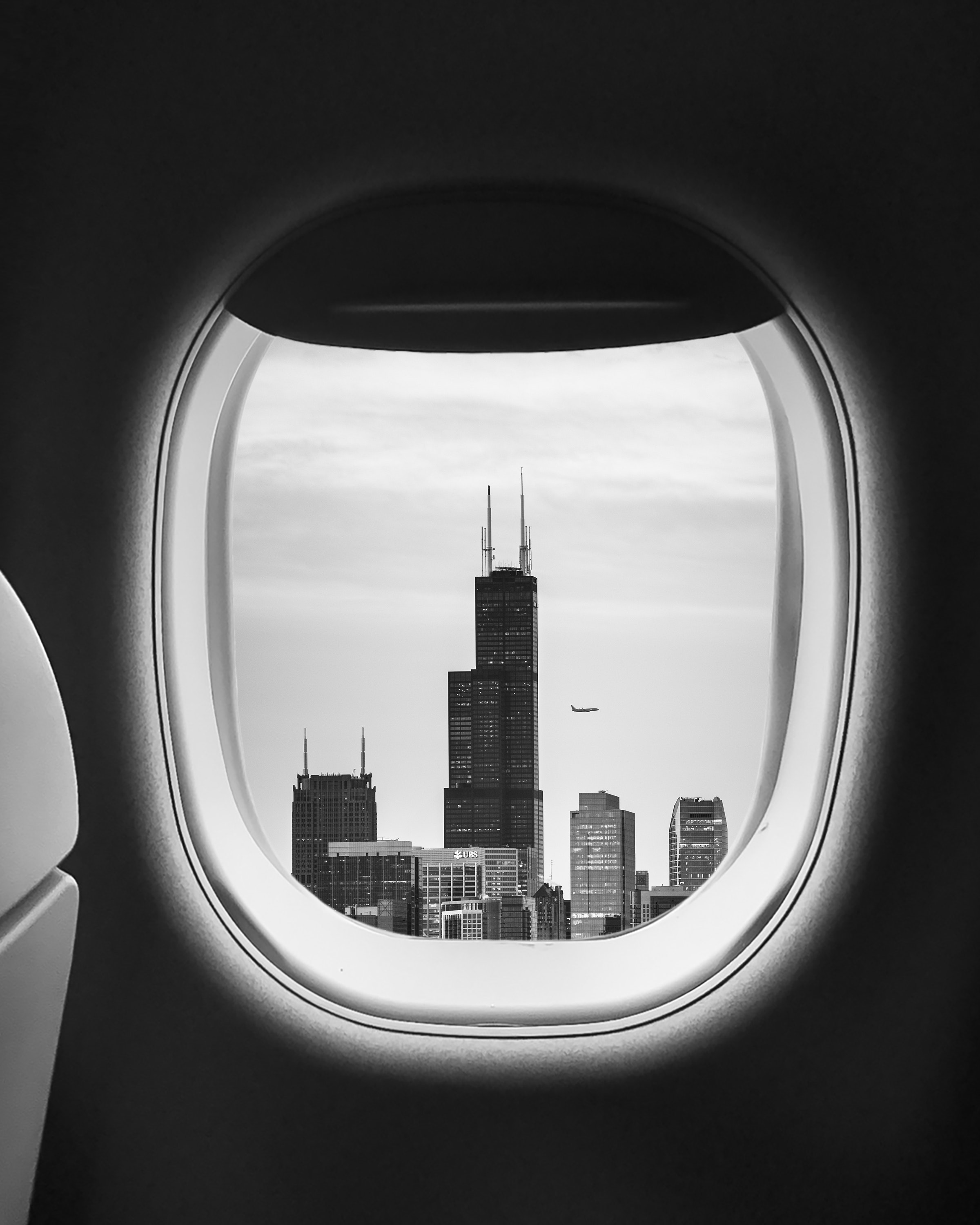 a window of an airplane with a tall building in the distance