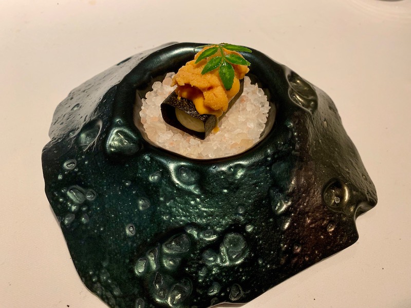 a black and white plate with a sushi roll and a leafy green leaf