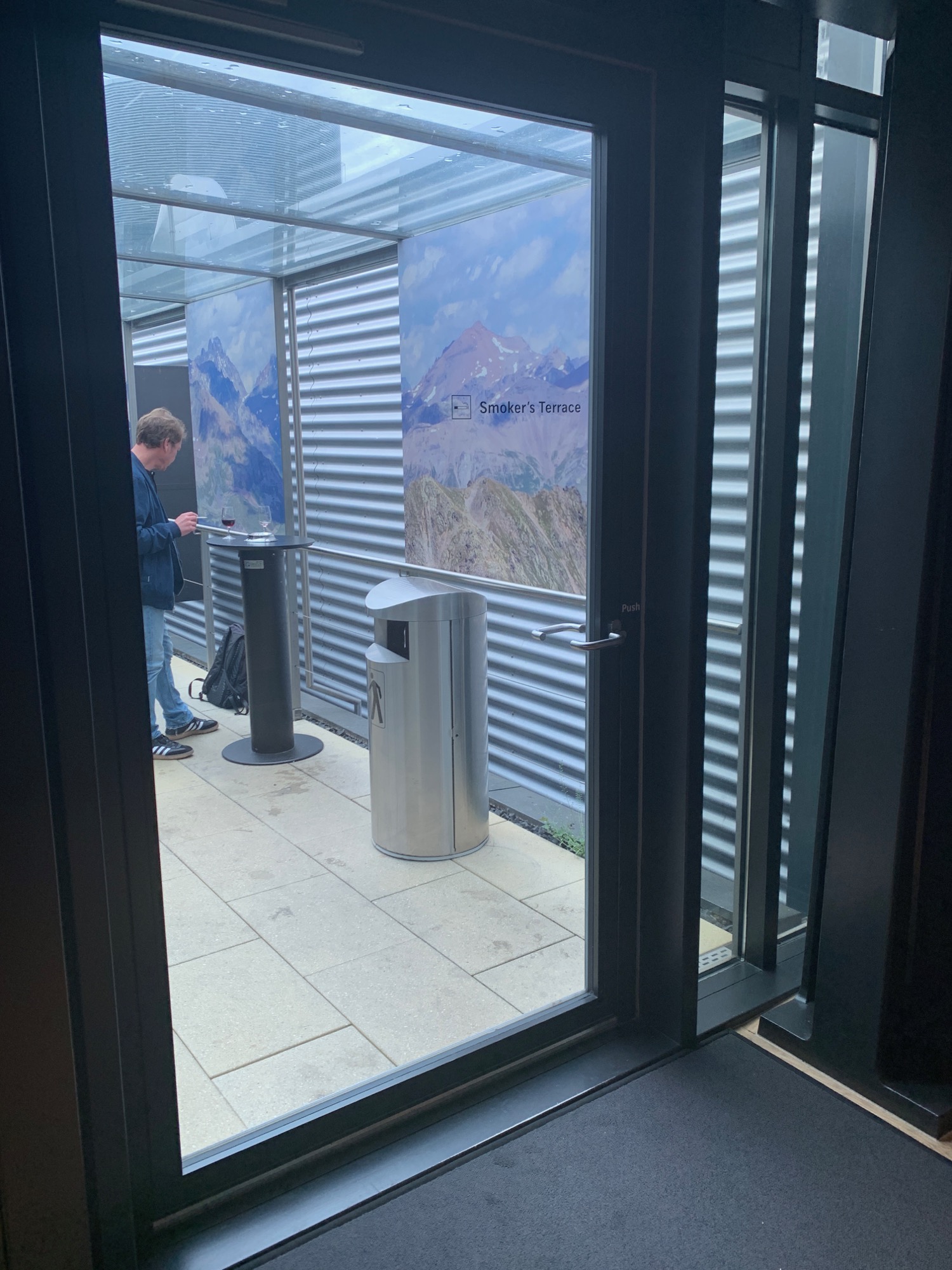 a glass door with a person standing in front of a silver trash can