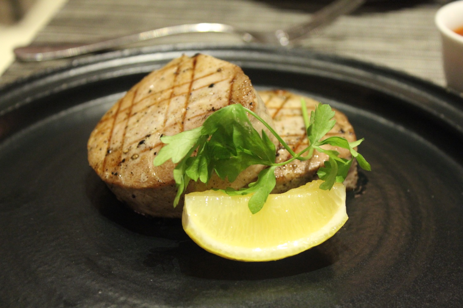 a piece of meat with a lemon wedge on a black plate
