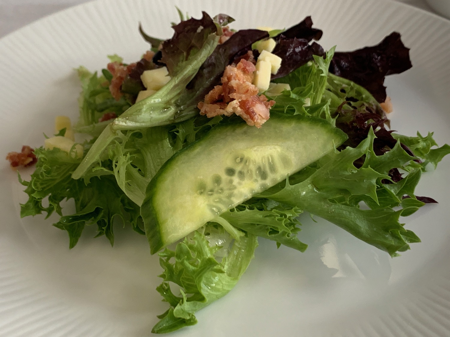a plate of salad with cucumber and bacon