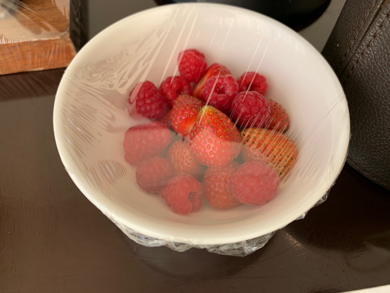 a bowl of raspberries and strawberries wrapped in plastic
