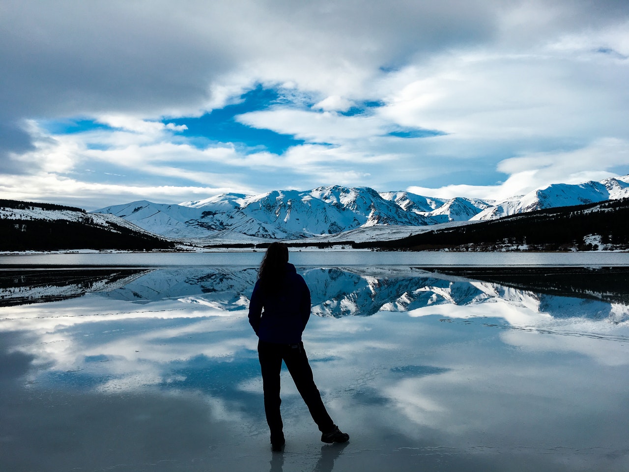 a person standing on a lake with mountains in the background