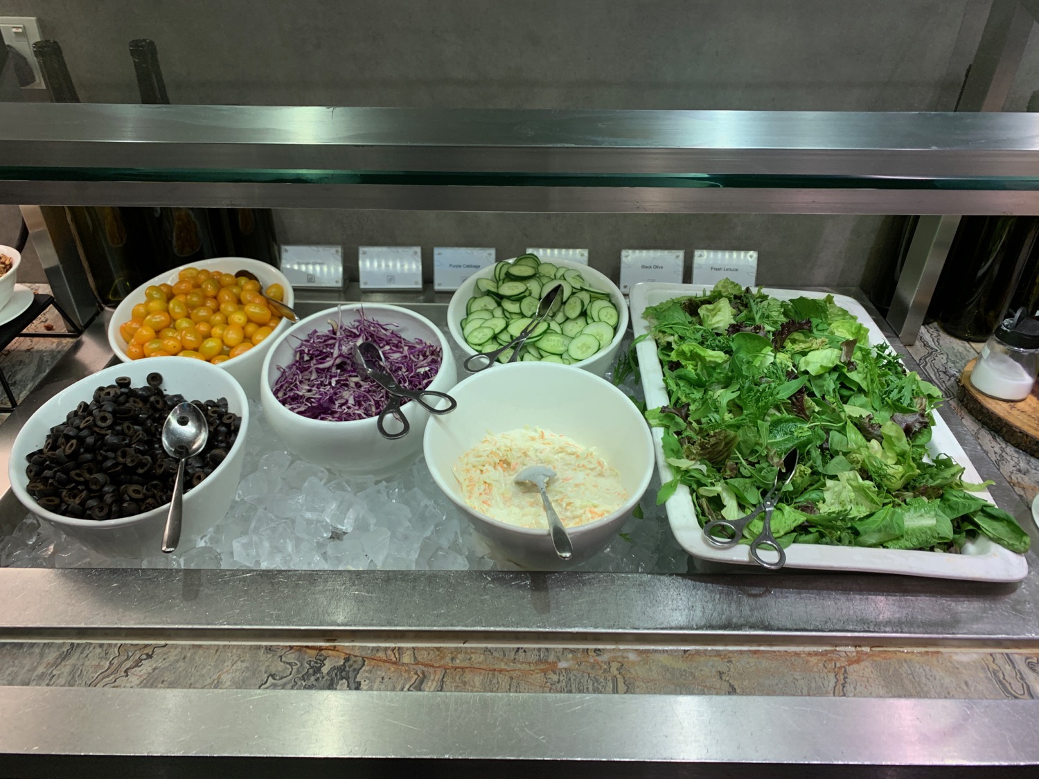 a salad bar with bowls of vegetables and olives