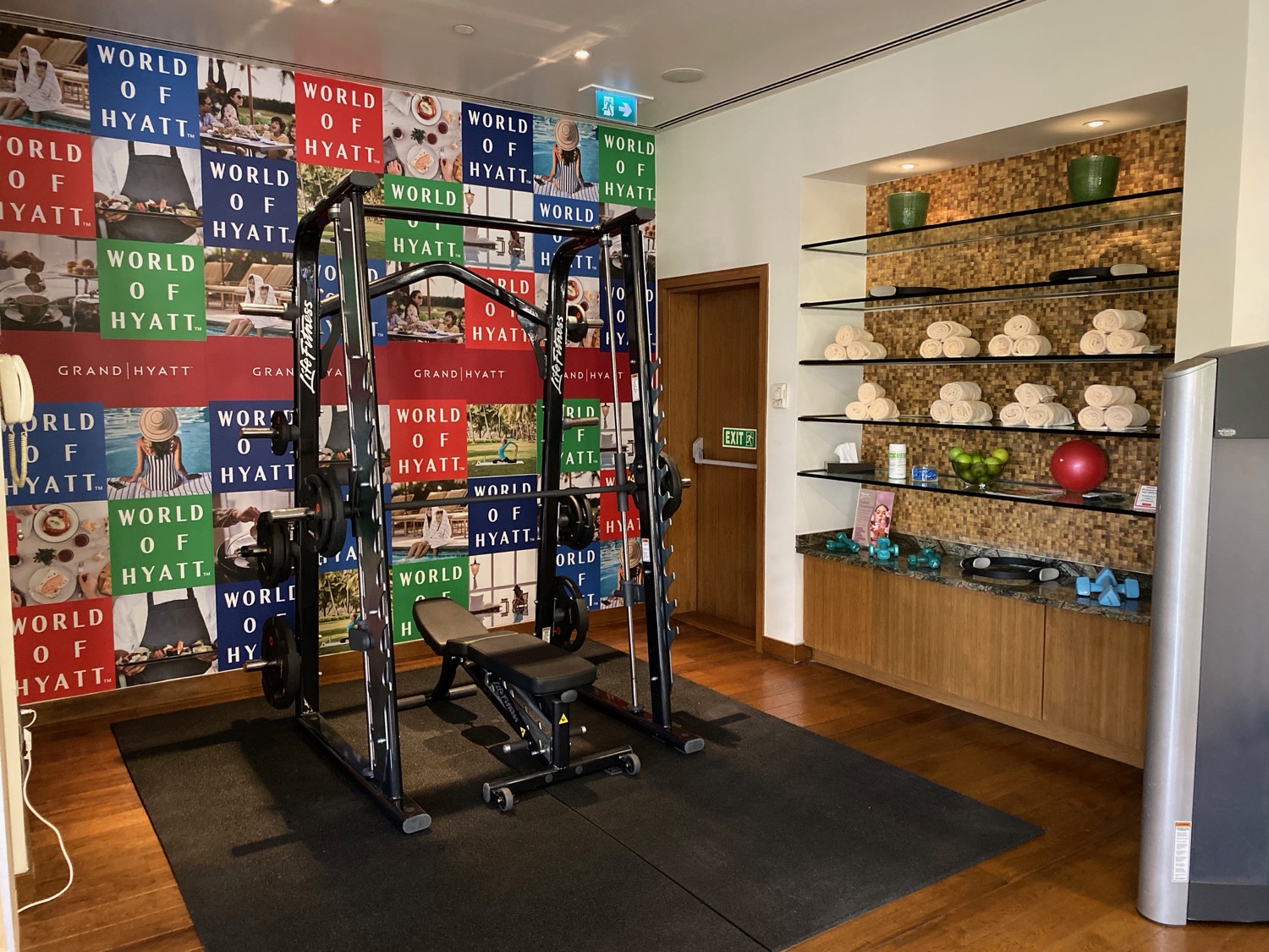 a gym with weights and a shelf with towels and a door