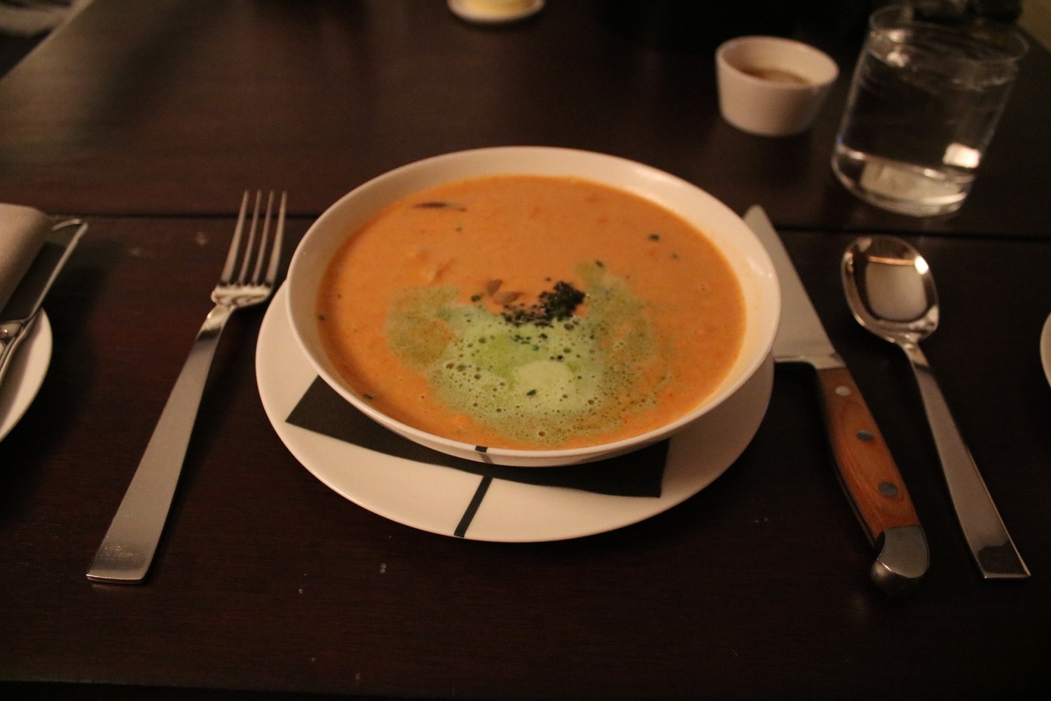 a bowl of soup on a plate with a fork and knife