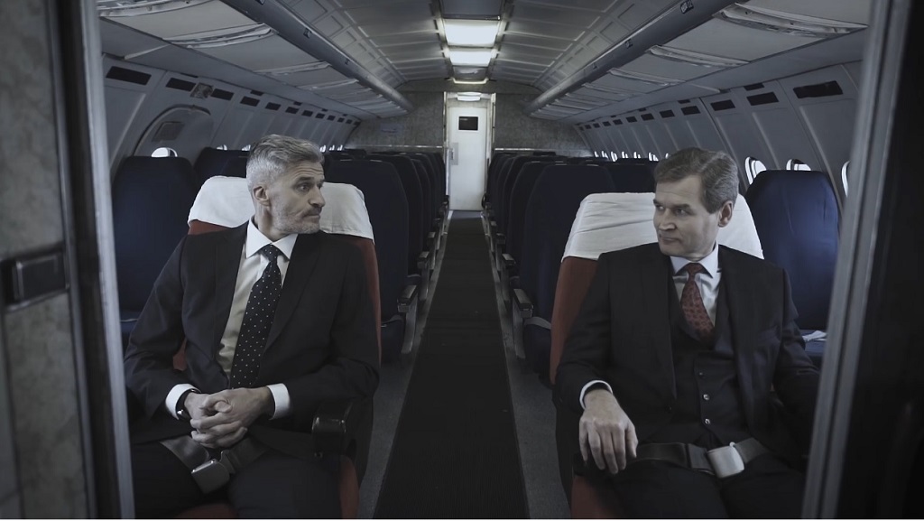two men in suits sitting in an airplane