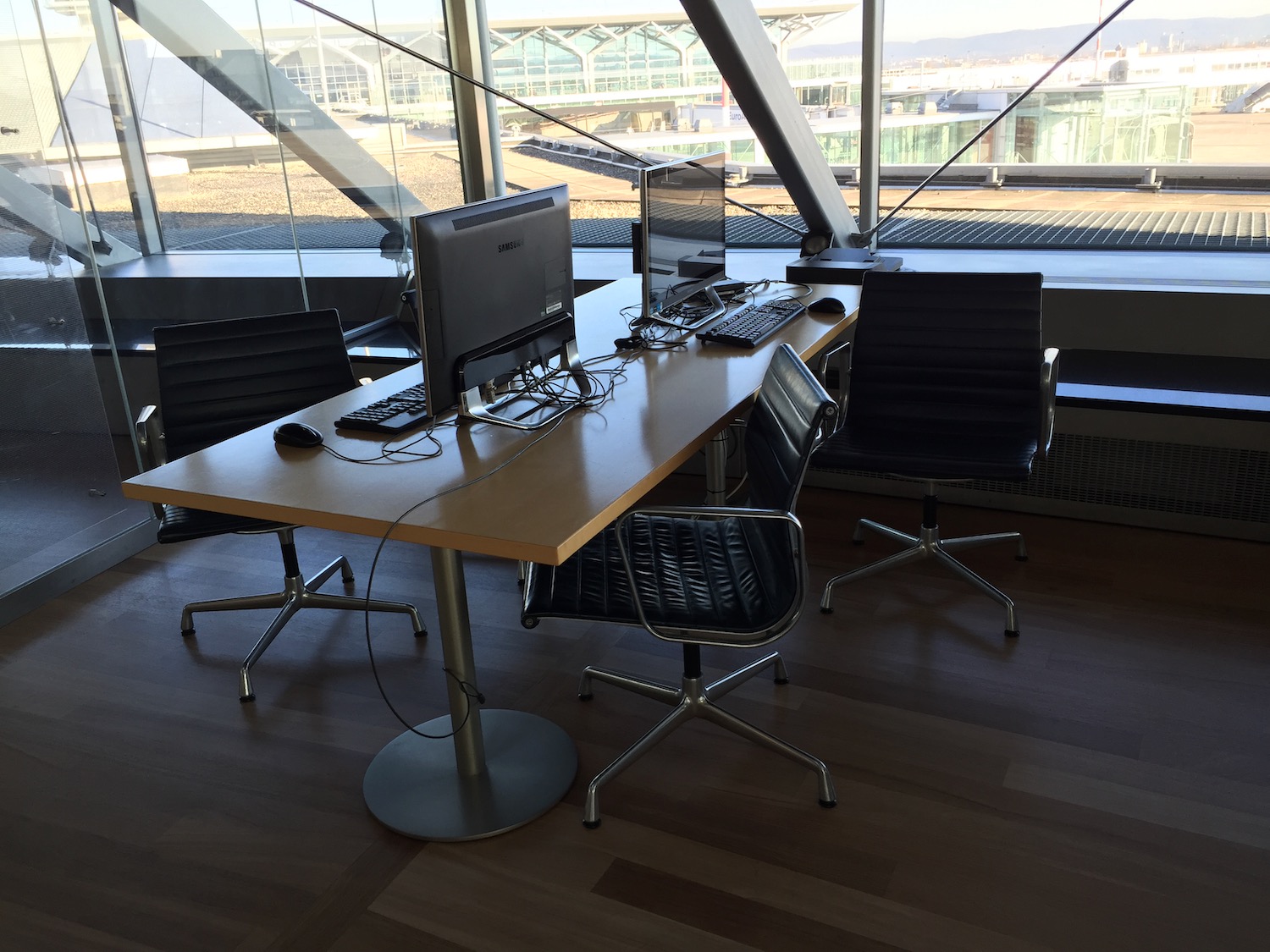 a desk with computers and chairs in a room with windows