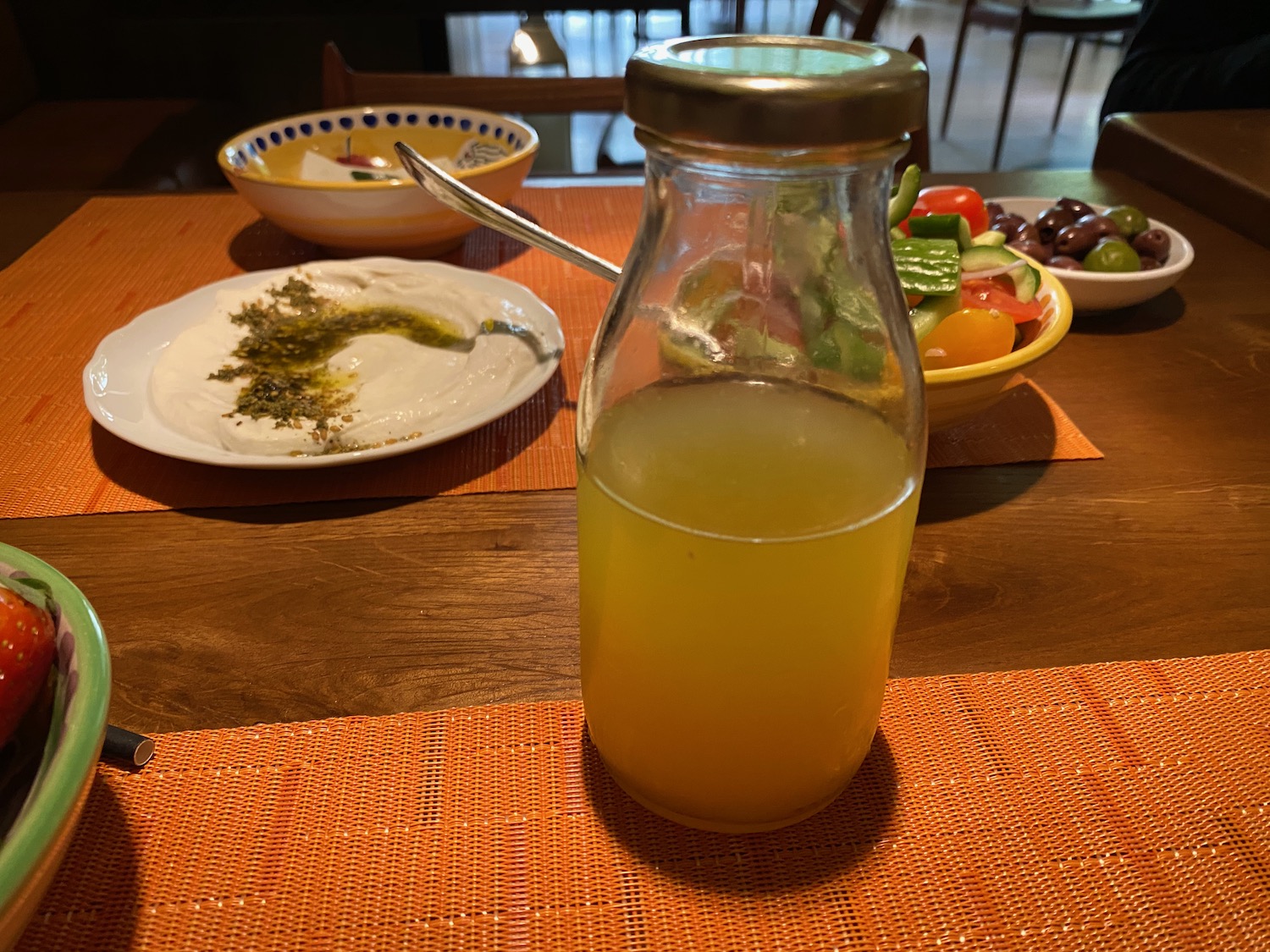 a glass bottle with yellow liquid on a table with a plate of food